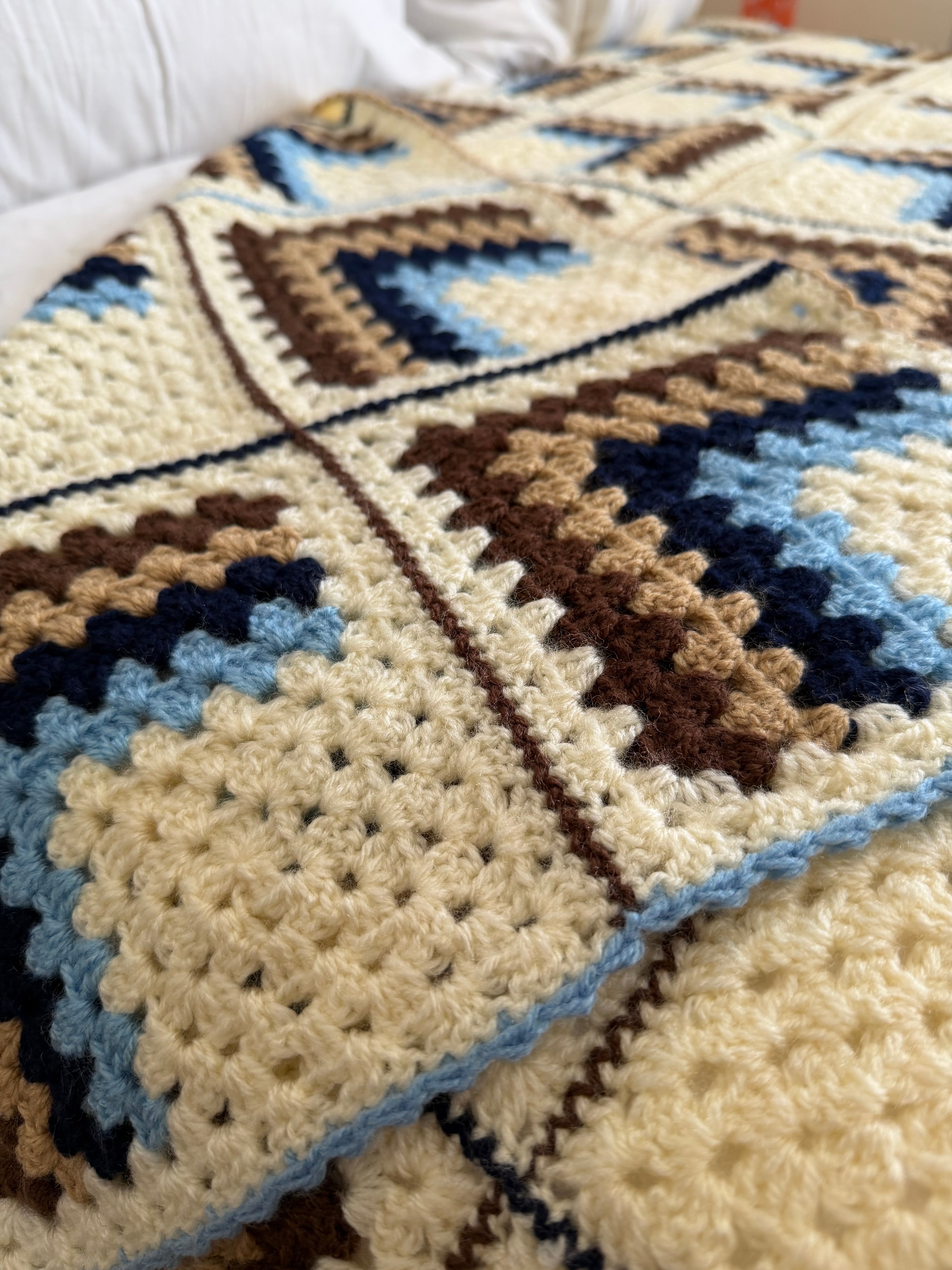 Close-up of a crocheted blanket with geometric pattern in beige, brown, and blue.